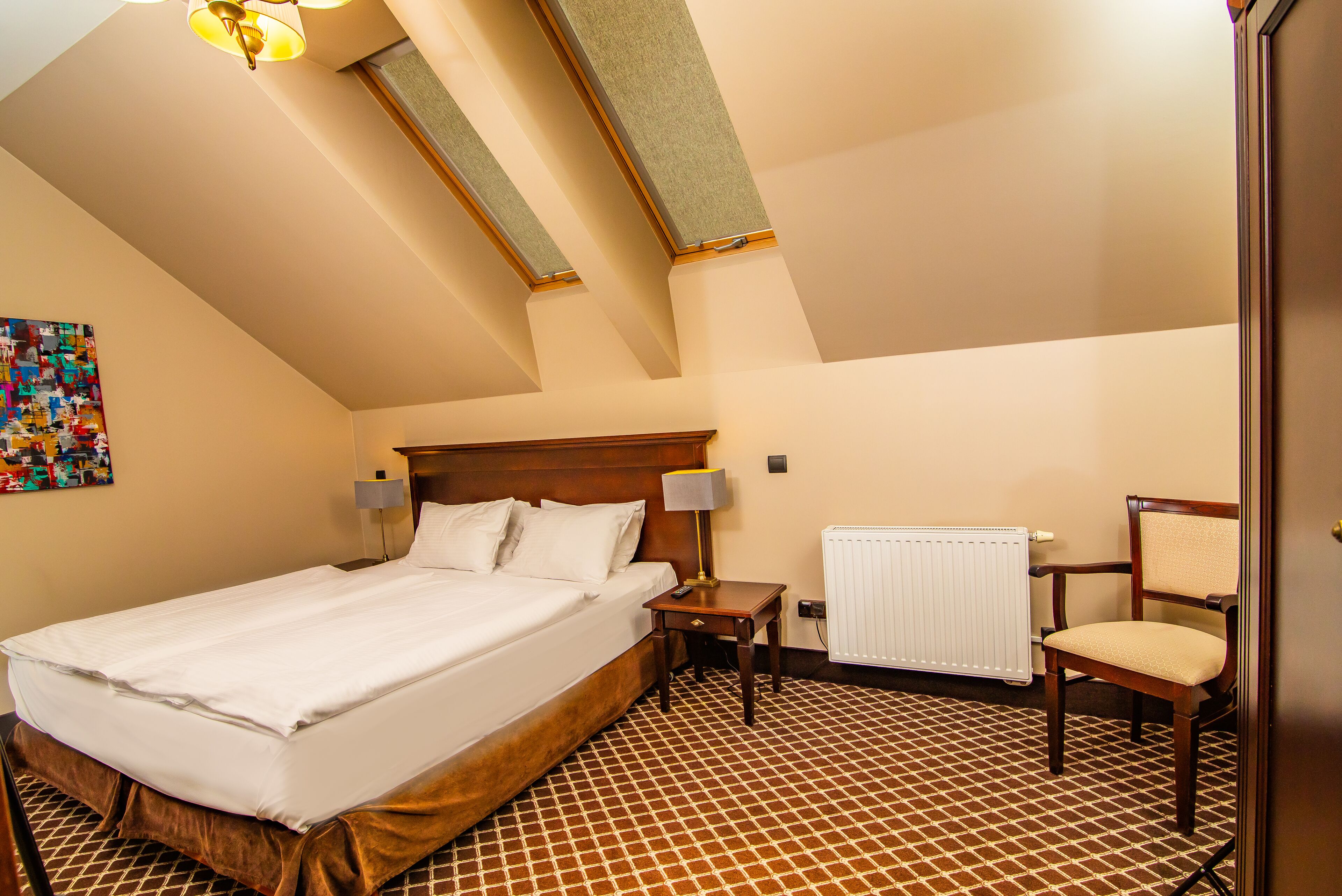 A hotel room with a large bed, a wooden nightstand, a chair, a lamp, and a radiator.