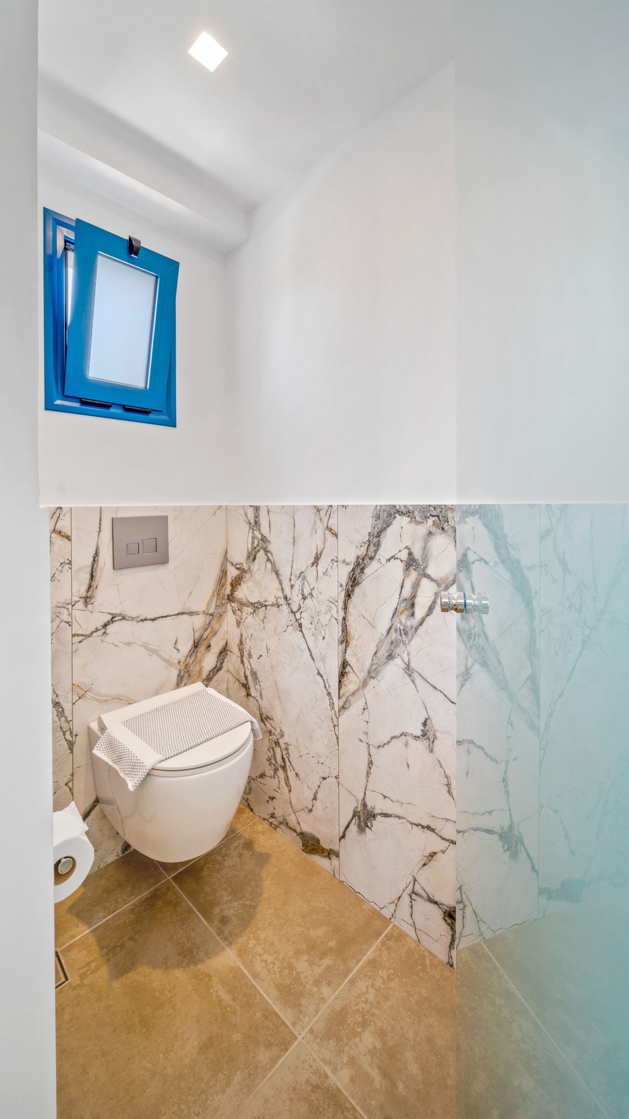Un baño con inodoro, paredes con diseño de mármol y un espejo con marco azul.