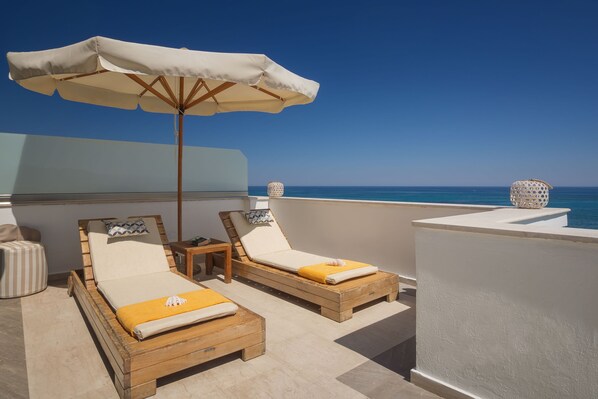 Un balcón con dos sillones de madera, una sombrilla blanca y vista al mar.