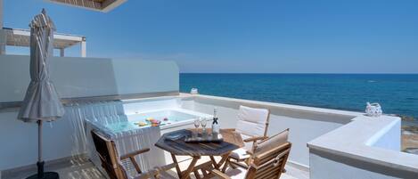 A balcony with a hot tub, wooden furniture, and a view of the sea.