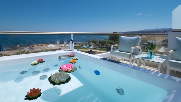 Un jacuzzi con flores de loto, una copa de vino y vista al mar.