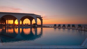 Una piscina con sillones de descanso y vistas al atardecer.