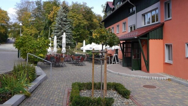 A courtyard with outdoor seating, a building with a red facade, and trees in the background.
