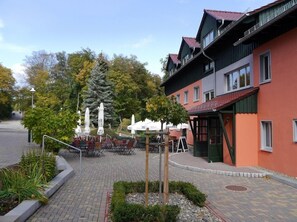 A courtyard with outdoor seating, a building with a red facade, and trees in the background. - AKZENT Berghotel Rosstrappe (Thale)