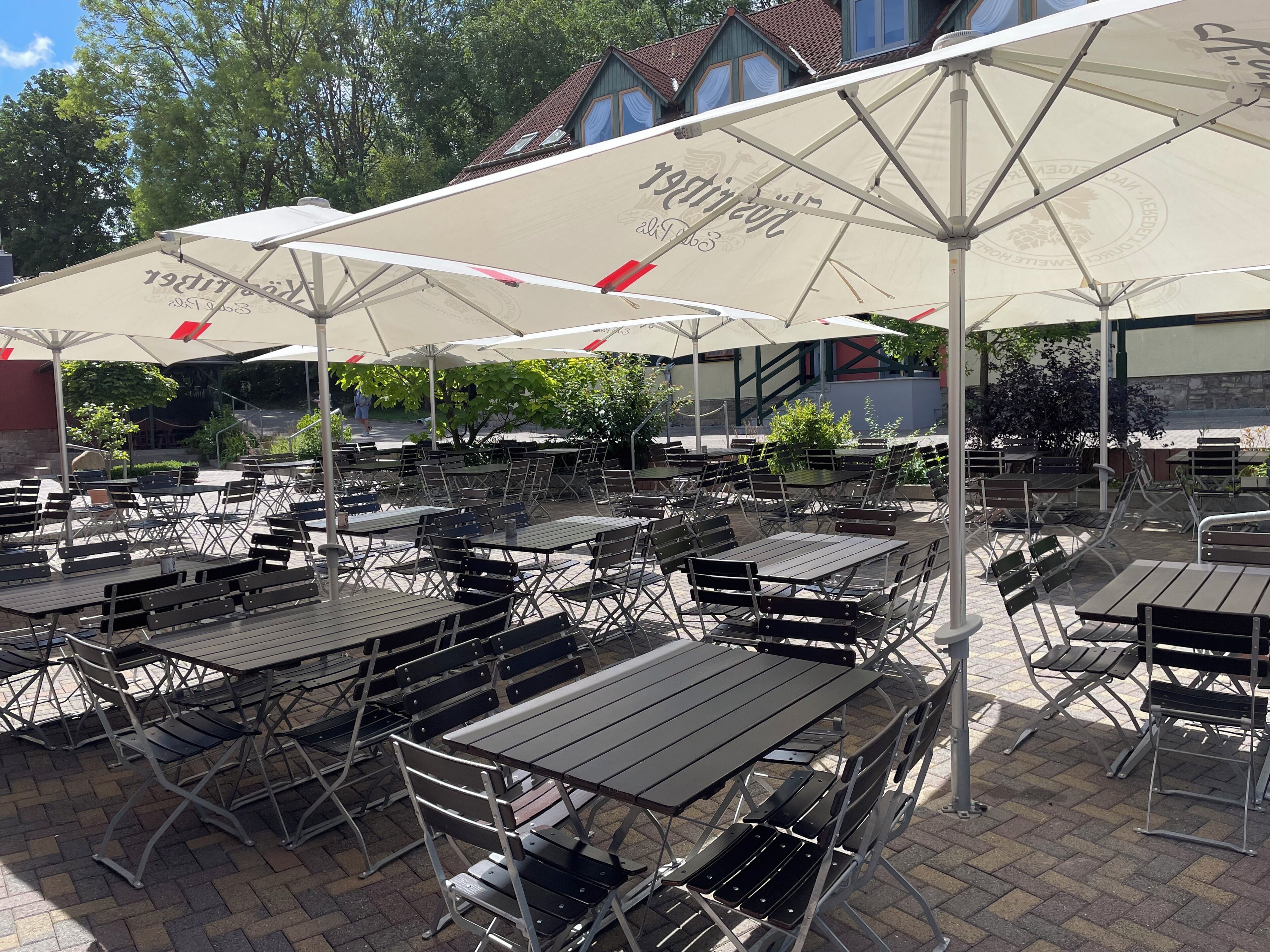 An outdoor seating area with tables and chairs, large umbrellas, and a building in the background.