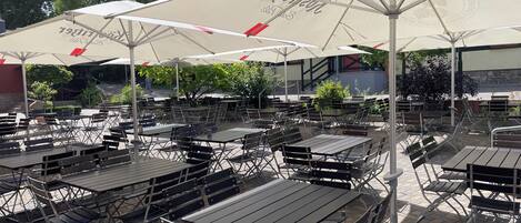 An outdoor seating area with tables and chairs, large umbrellas, and a building in the background.