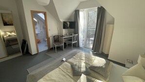 A bedroom with a bed, a desk, a chair, a TV, and a balcony with curtains.
