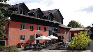 A building with multiple windows and a red facade, outdoor seating with umbrellas, and a sign indicating a beer garden.