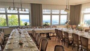 A long dining table set with white tablecloths, silverware, and glassware, surrounded by upholstered chairs.