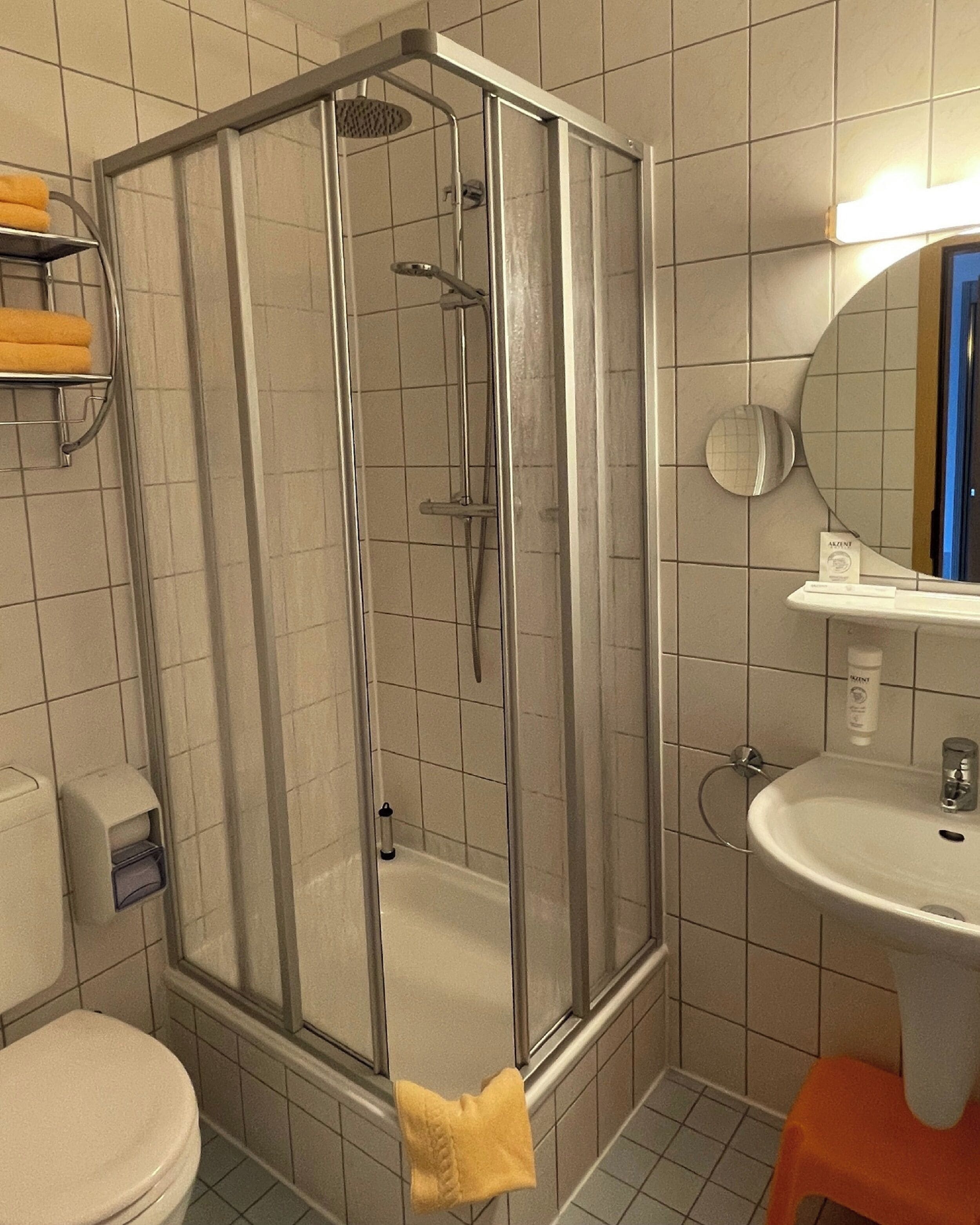 A bathroom with a glass-enclosed shower, a white sink, a toilet, and a mirror.