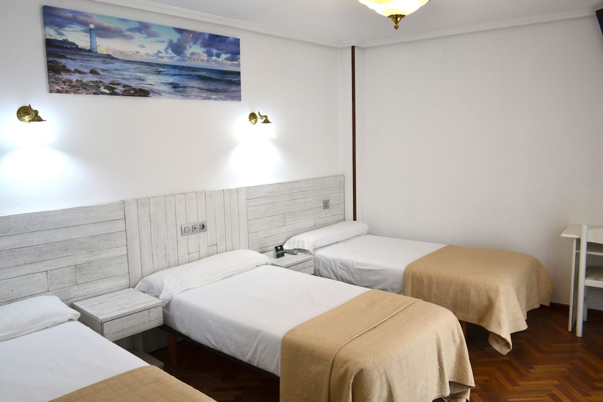 A hotel room with two single beds, a wooden headboard, a nightstand, a lamp, and a painting of a lighthouse on the wall.