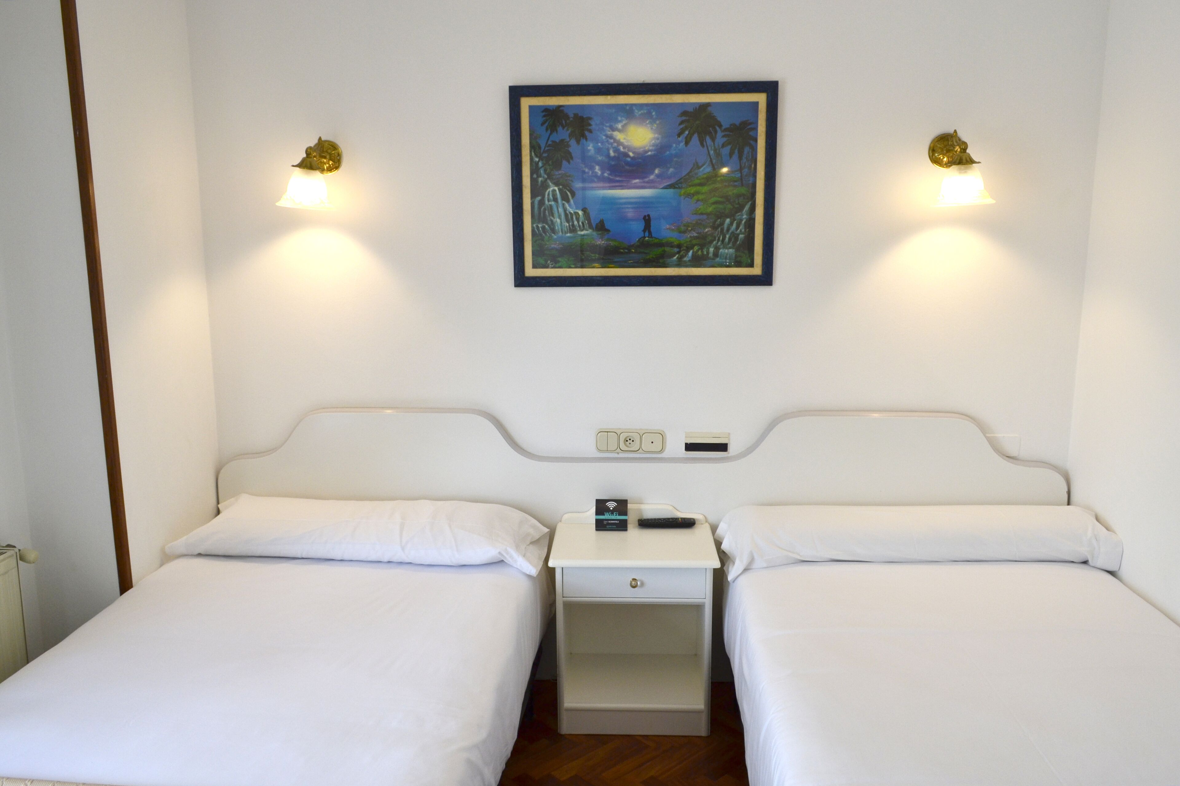 Una habitación de hotel con dos camas individuales, una mesita de noche con un control remoto y un cuadro en la pared.