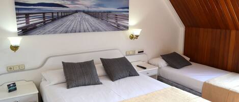 A hotel room with two beds, a wooden ceiling, a painting of a pier, and a nightstand with a lamp.