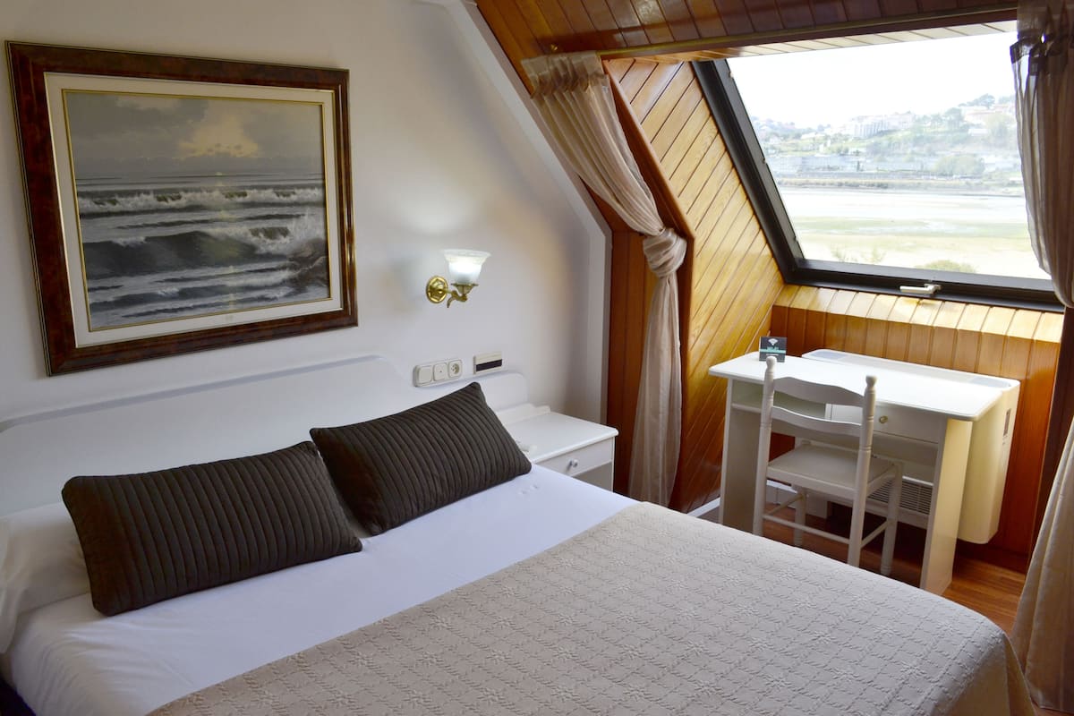 A bedroom with a bed, a desk, and a window with a view of the sea.