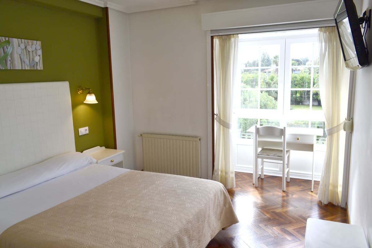 A bedroom with a bed, a nightstand, a radiator, a chair, and a window with curtains.