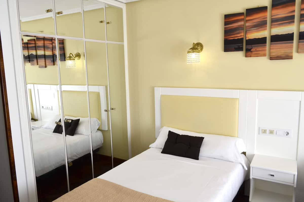 A hotel room with a large bed, a bedside table, and a mirror.