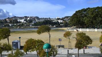 Vista de la playa con un paseo pavimentado, árboles y un pueblo distante.