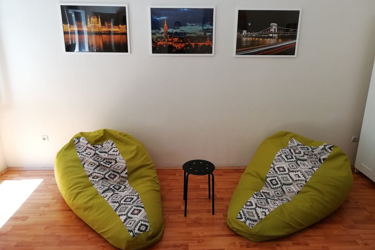 Una habitación con dos puffs, un taburete pequeño y tres cuadros en la pared.