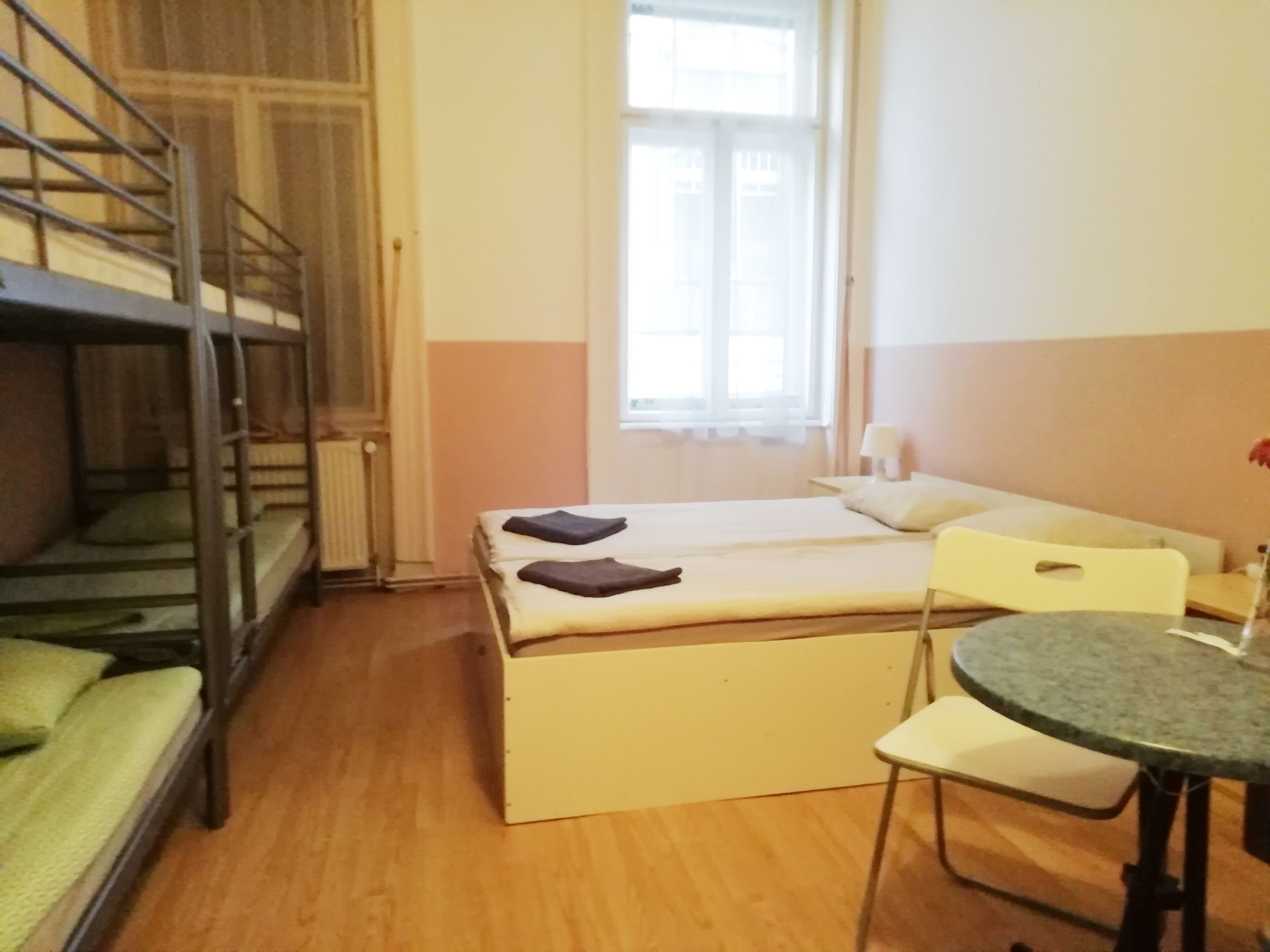 A dormitory room with bunk beds, a single bed, a small table, and a chair.