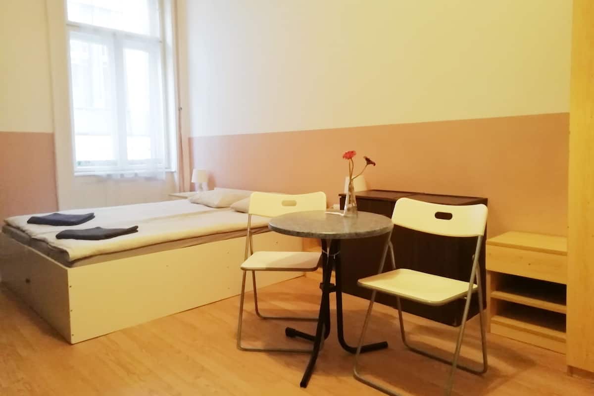 Una habitación pequeña con una cama, una mesita redonda, dos sillas y una ventana.