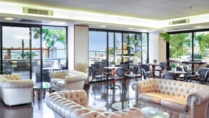 A spacious lounge area with leather sofas and chairs, large windows offering a view of the beach, and a dining area with tables and chairs. - Milano Resort (Bellaria-Igea Marina)