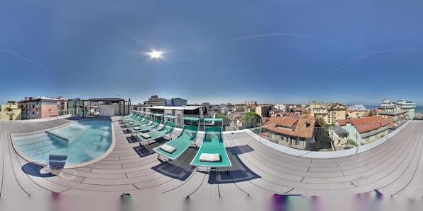 A rooftop swimming pool with lounge chairs and a sun deck, overlooking a cityscape.