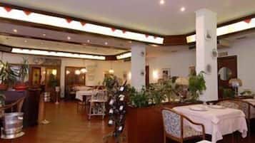 Un restaurant doté de nombreuses tables et chaises, de plantes en pot et d’un sol carrelé.