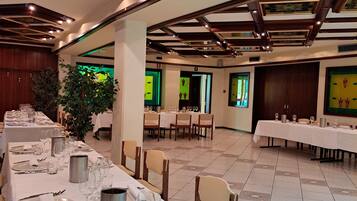 A banquet hall with long tables set for dining, wooden beams on the ceiling, and a large plant in the center.