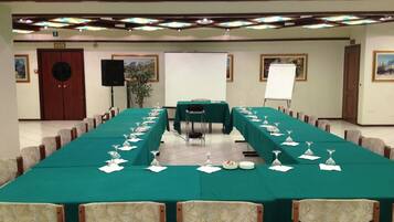 A conference room with a long table, chairs, a projector screen, and a speaker.