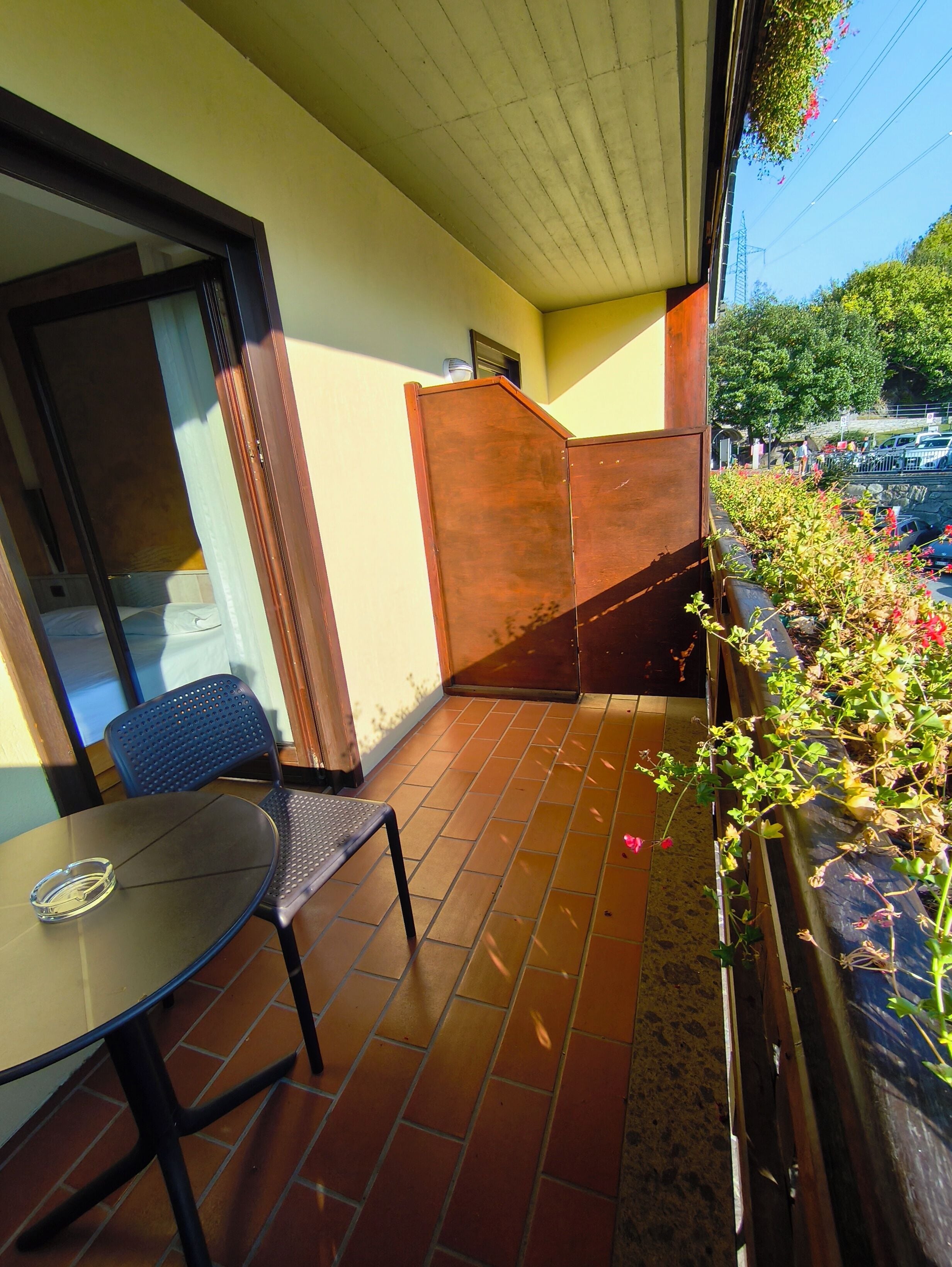 Un balcón con mesa y silla, una puerta de madera y vista a la calle.