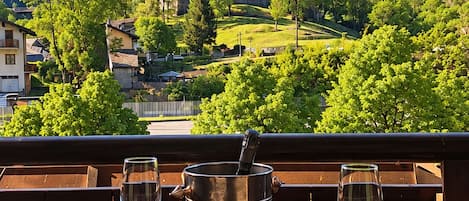 A table with two wine glasses on a balcony overlooking a mountainous landscape with a castle.