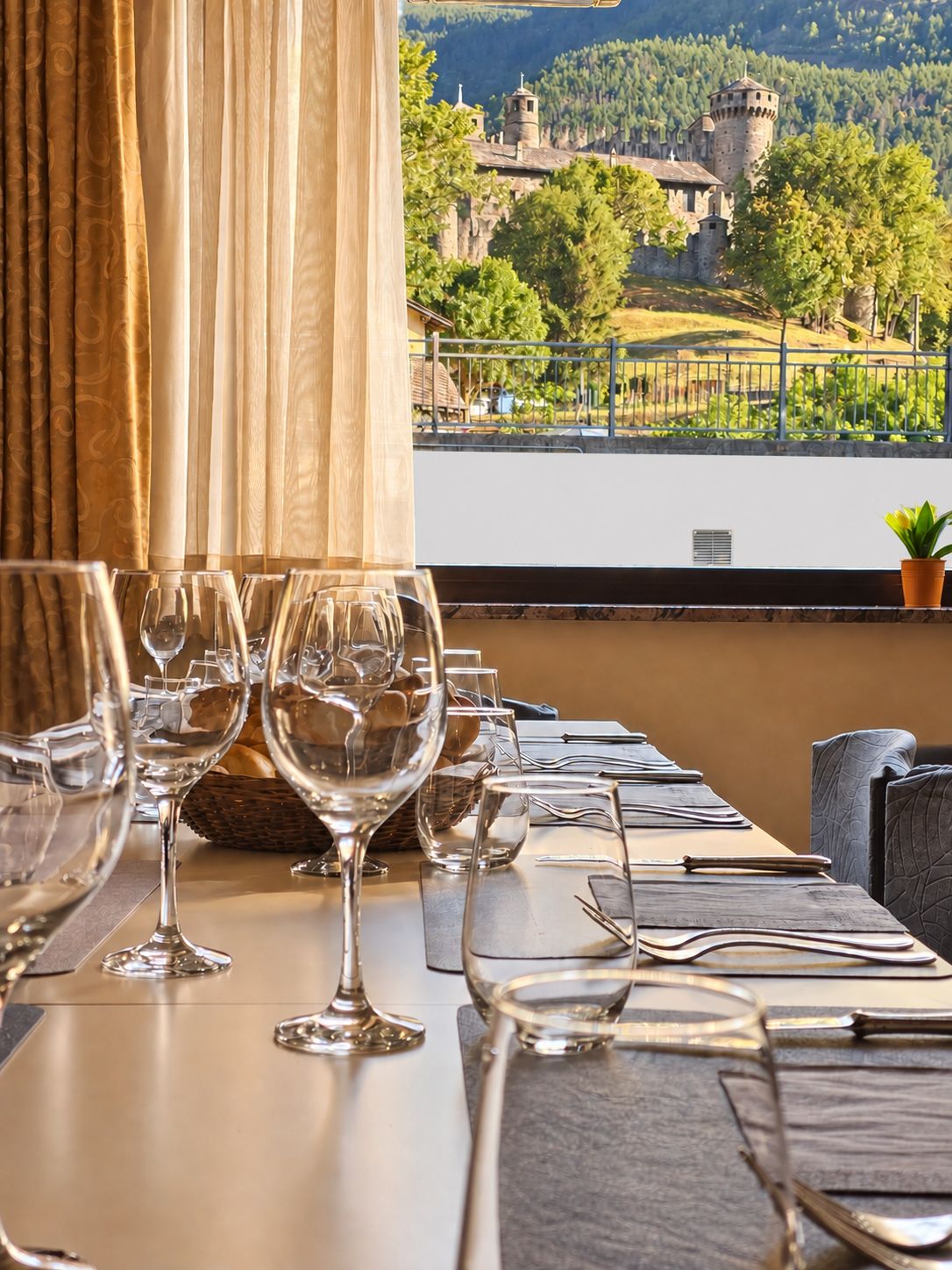 A dining table set with wine glasses, cutlery, and a view of a castle through a window.