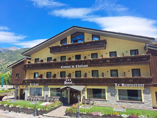Un hotel con fachada amarilla, balcones con jardineras florales y un letrero que dice 'Comtes de Chavallaz Hotel'.