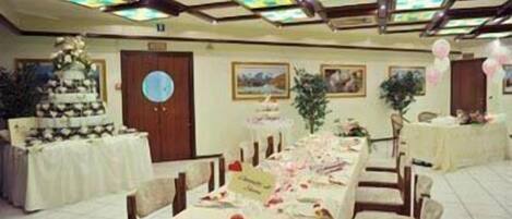 A banquet hall with long tables set for a formal event, decorated with floral arrangements and a tiered cake.