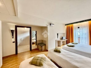 A hotel room with two beds, a desk, a mirror, a small seating area, and a window with curtains. - Comtes de Challant (Fenis)