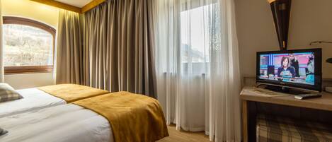Una habitación de hotel con dos camas, televisión, ventana con cortinas y una lámpara.