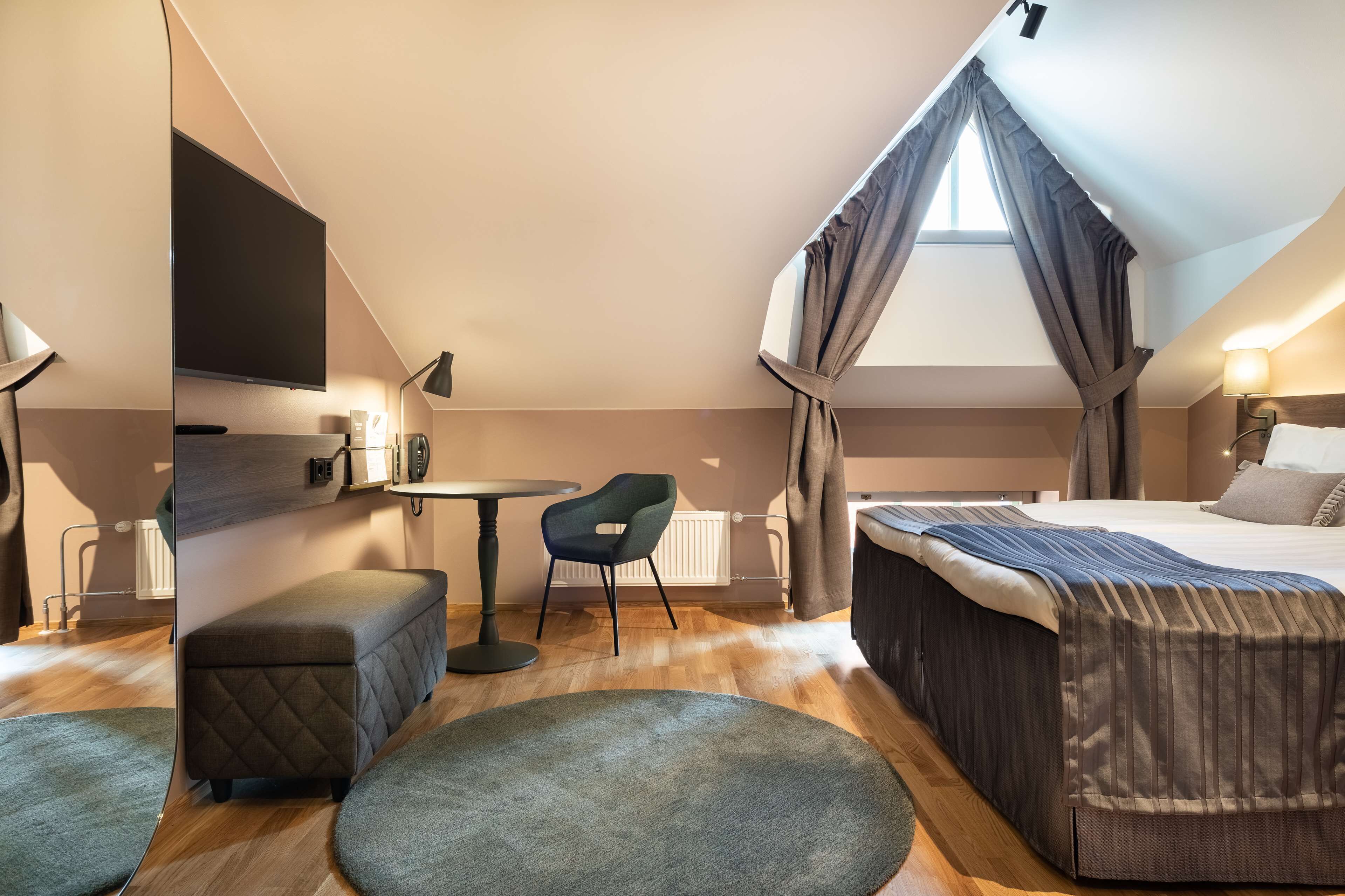 Una habitación pequeña y bien iluminada con una cama, una mesita, una silla y un banco.