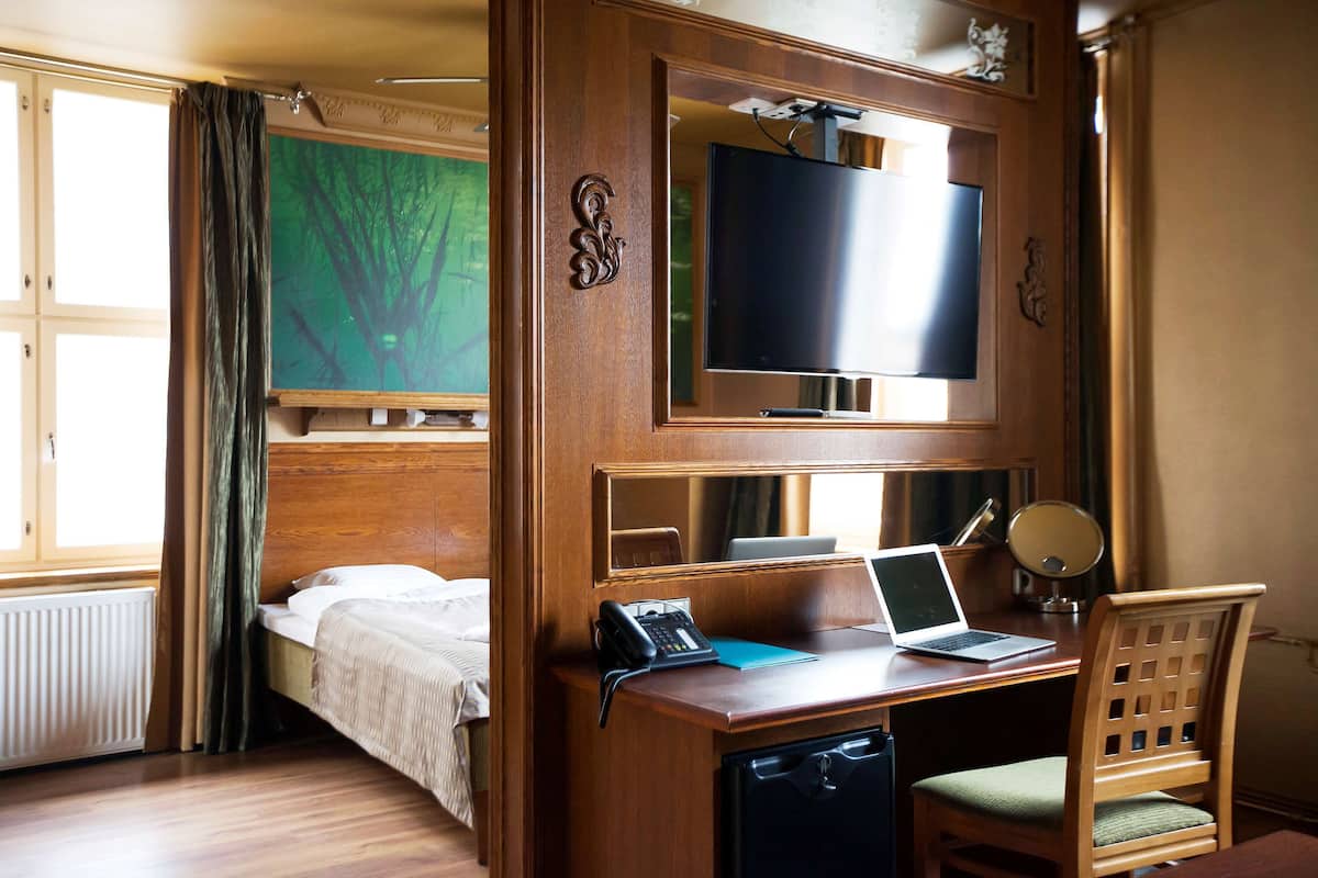 Una habitación de hotel con una cama, un escritorio con una computadora portátil, un teléfono y un televisor.