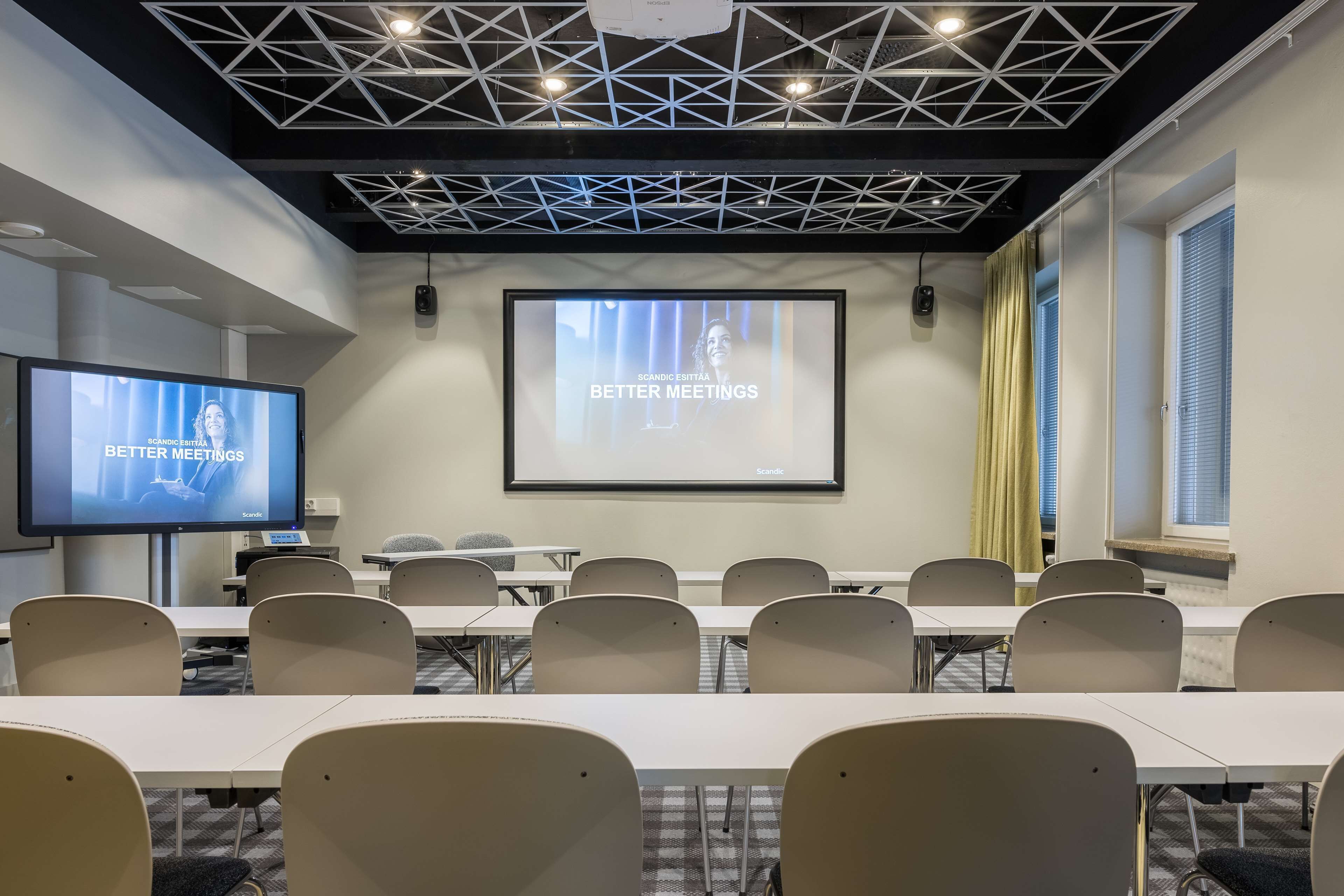 A conference room with a large screen, multiple tables, and chairs.