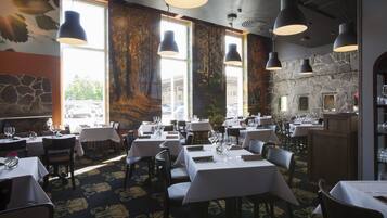 A restaurant interior with multiple tables, hanging pendant lights, and a stone wall.