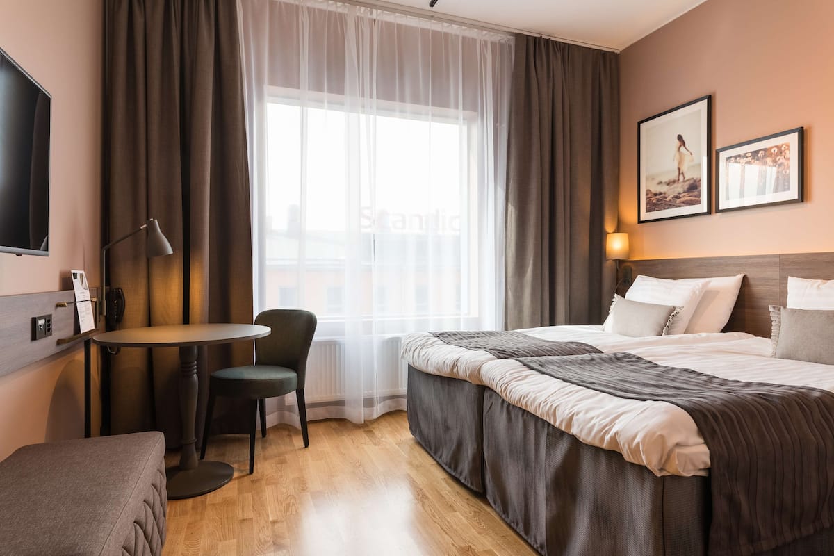 Habitación de hotel con una cama, escritorio, silla, televisor y ventana con cortinas.