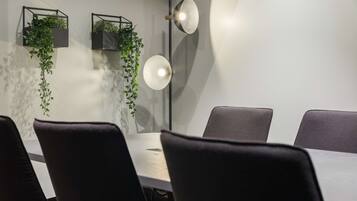 Une salle de conférence avec une table blanche, des chaises noires et deux jardinières noires suspendues, dans lesquelles se trouvent des plantes vertes.