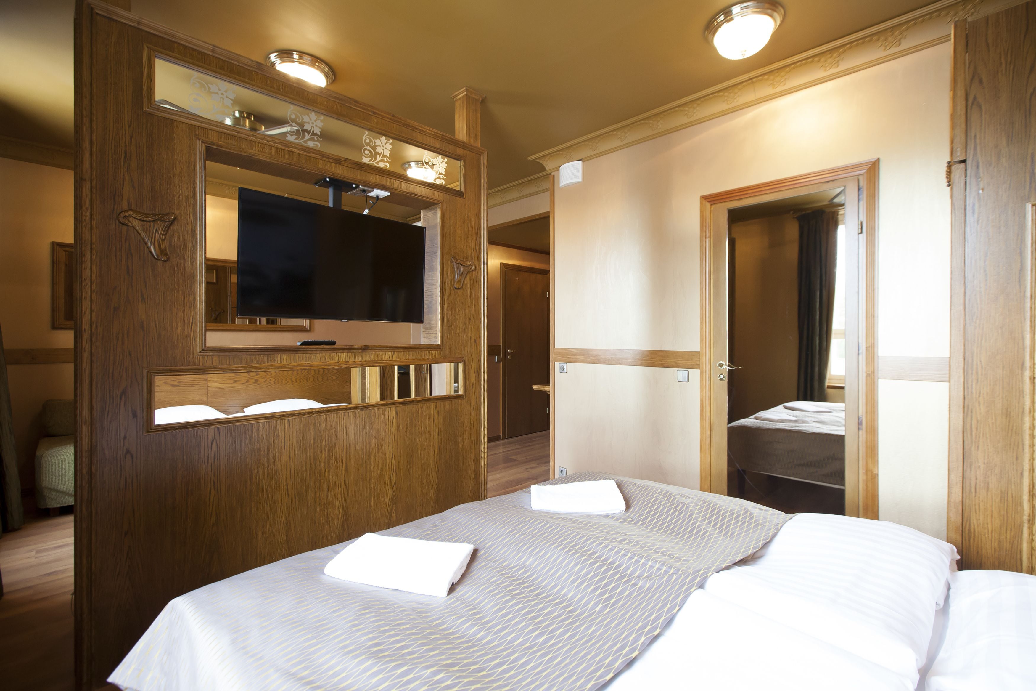 Een hotelkamer met een groot bed, een televisie, een houten kledingkast en een spiegel.