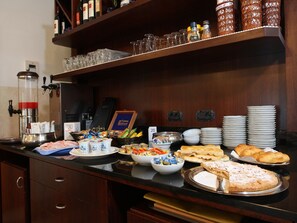Una mesa de buffet con diversos alimentos, como pasteles, una máquina de café y salsas.