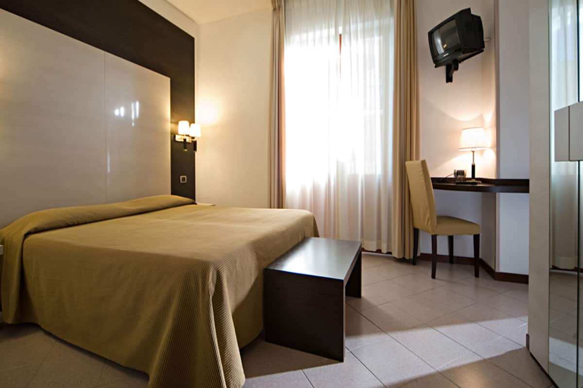 Een hotelkamer met een bed, een bureau, een stoel, een televisie en een raam met gordijnen.