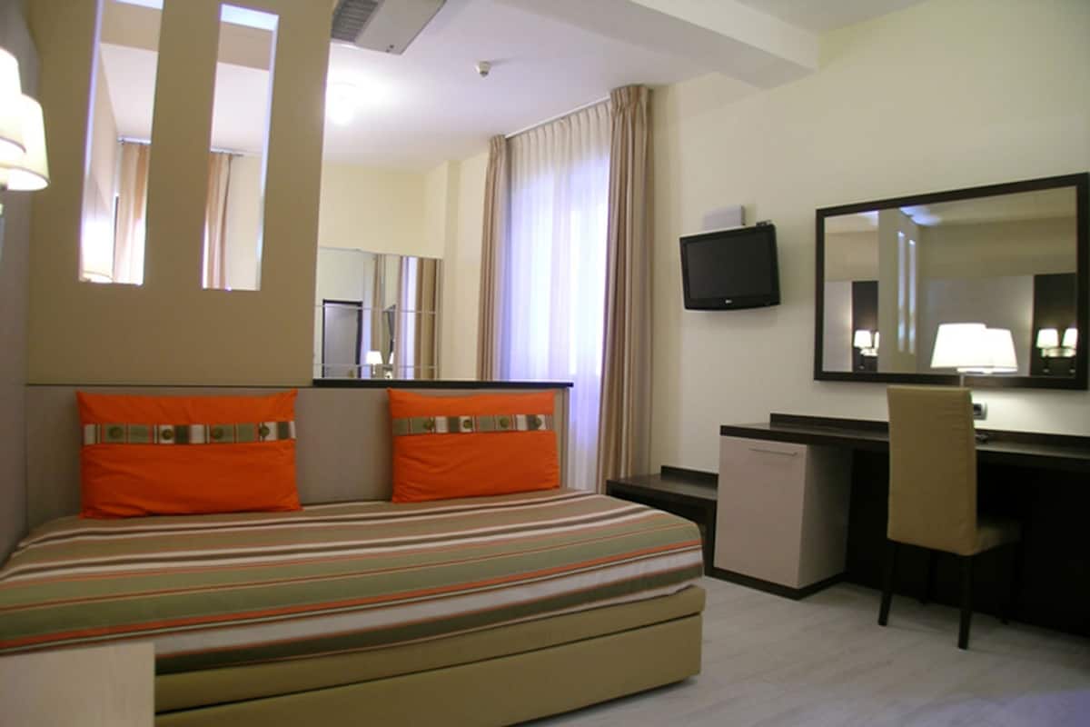 Een hotelkamer met een bed, een bureau, een stoel, een televisie en een spiegel.