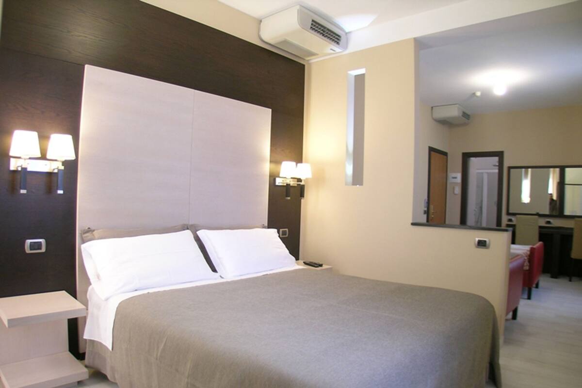 Een hotelkamer met een bed, bedlampjes, een bureau en een spiegel.