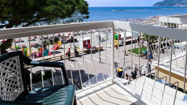 A beachside seating area with a view of the sea and a tree line. - Hotel Anita (San Bartolomeo al Mare)