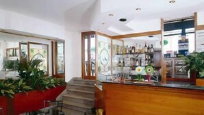A modern interior with a wooden reception desk, a seating area with chairs, and a staircase leading to an upper level. - Hotel Anita (San Bartolomeo al Mare)