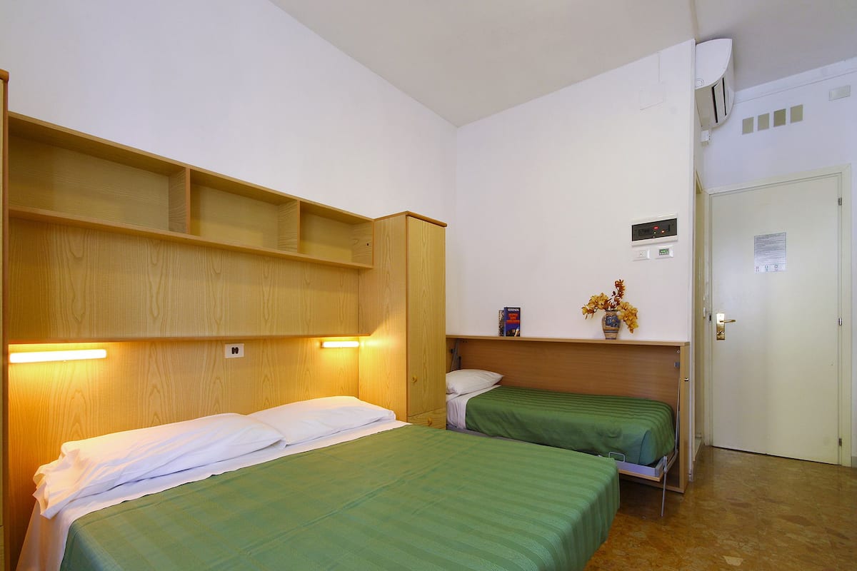 Ein Zimmer mit zwei Betten, Holz-Kopfteilen, einem Regal mit einer Blumenvase und einer Tür mit einem Schild.
